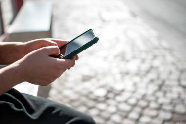Sokakta arka planda oturan ve cep telefonu kullanan ellerin yakın görüntüsü