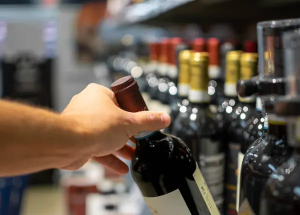 Image of Hand taking bottle of wine stocked on supermarket for selling and ready for consumption