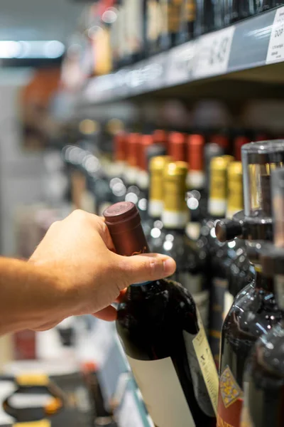 Image of Hand taking bottle of wine stocked on supermarket for selling and ready for consumption