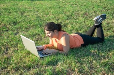 Kafkasyalı genç bir kadının laptopuyla parkta yatması çok mutlu bir görüntü.