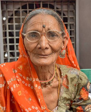 Arka planda harabelerle poz veren güzel yüzlü ve turuncu elbiseli Hintli kadın. Rajasthan, Hindistan.