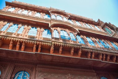 View of Dulmera Havelis in Bikaner with windows in green tones and touristy red facades, India. clipart