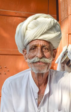 Geleneksel Rajasthani türbanlı yaşlı adam arka planda sıcak turuncu tonları olan kameraya mutlu bir şekilde bakıyor.