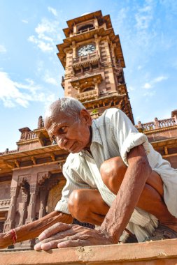 Hindistan, Jodhpur 'da çömelmiş, saat karesinin altında beyaz saçlı, kahverengi tonları olan yaşlı Hintli bir adam..