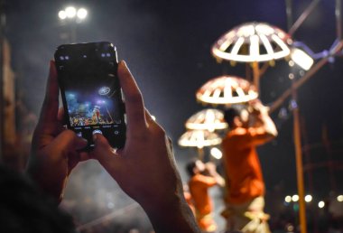 Ganj nehri kıyısındaki Aarti töreninde telefonla fotoğraf çeken eller görülüyor..
