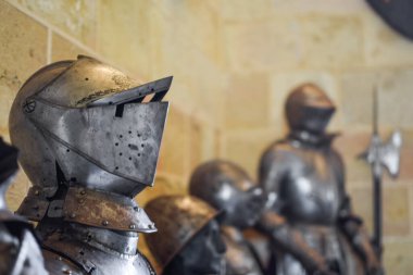 Ortaçağ parlak miğferinin detaylarla ve kireçtaşı duvar arka planındaki diğer zırhlarla yan görüntüsünü kapatın. Segovia, İspanya.