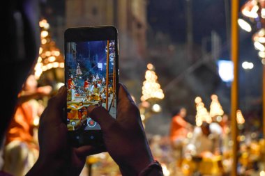 Ganj nehri kıyısındaki Aarti töreninde telefonla fotoğraf çeken eller görülüyor..