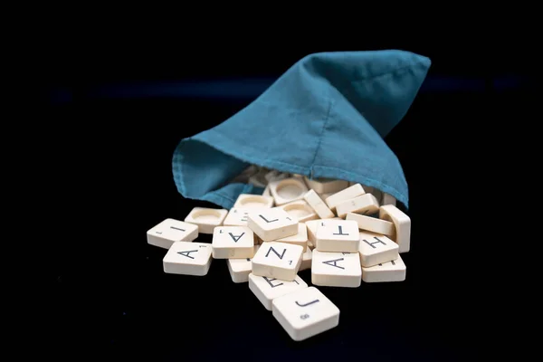 scrabble letter tiles coming out of a green bag. Black background