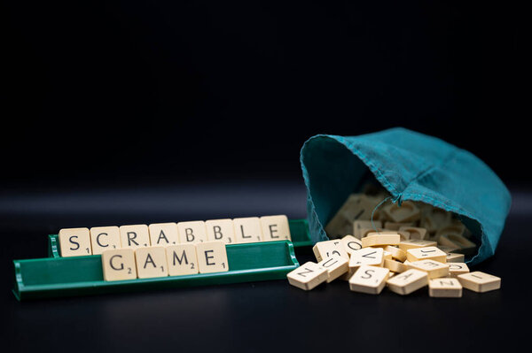 Настольная игра Эрудит. Слово Scrabble от буквы плитки в стойке плитки на черном фоне с выдвижной буквы мешок. Снимок студии.
