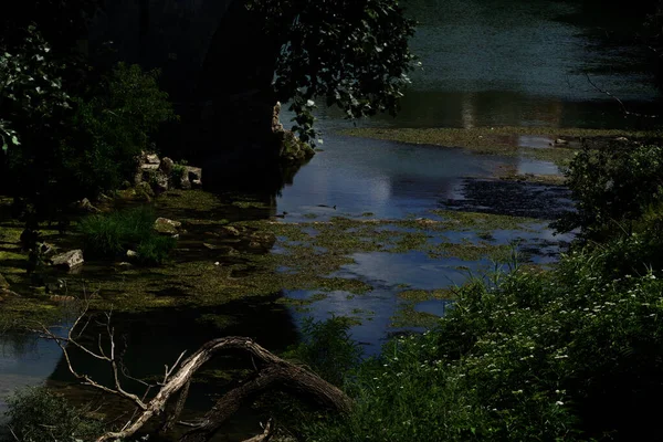 古代ローマ時代の橋の下を流れるロマンチックな植物に覆われた小川 — ストック写真