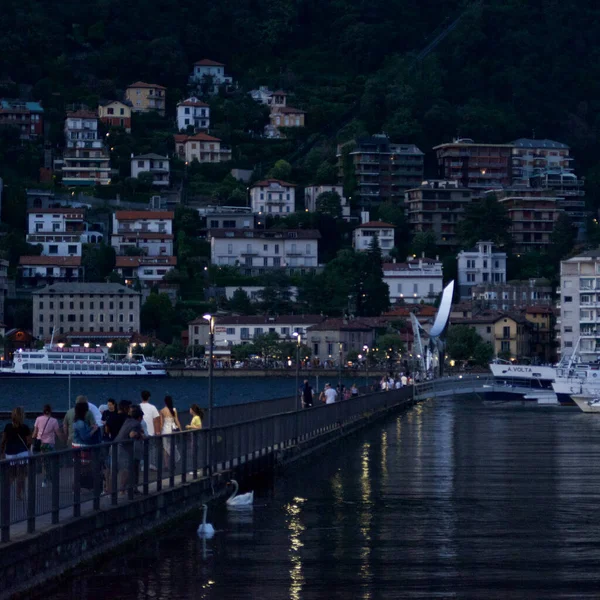 Como, İtalya - 20 Haziran 2023: turistler arka planda gölle birlikte antik Como şehrinin sokaklarında gece vakti geziniyorlar.