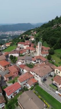 Yükselen uçakla dikey yörünge görüntüsü, eski yeşil ağaçlarla çevrili Como Gölü 'ndeki Ponzate kasabasındaki St. Brigid Kilisesi' nin çan kulesini gözler önüne seriyor.