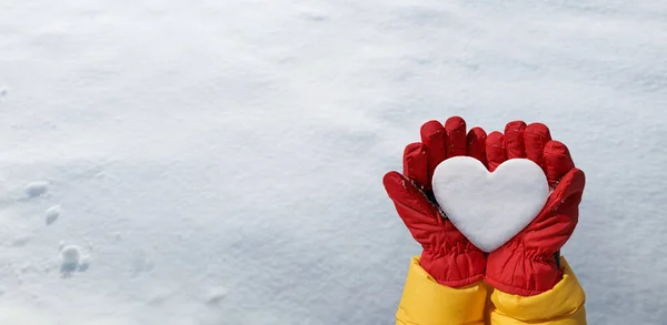 Panoramic view of hand in red glove holds snow heart on snow background. Romantic winter lovers concept