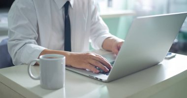 Yanında kahve fincanı olan bir dizüstü bilgisayarda, ofis ortamında daktilo eden bir profesyonelin yakın çekimi.