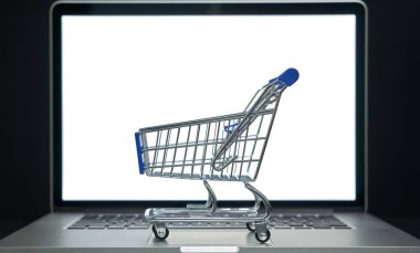 Küçük alışveriş arabası, e-ticaret ve dijital alımı temsil eden bir dizüstü bilgisayarın önünde sergileniyor
