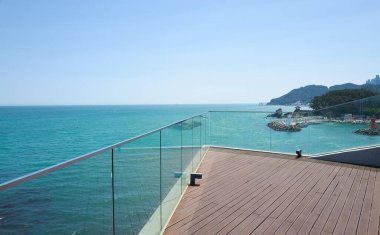 Günümüz ahşap terası, sakin mavi bir deniz ve güneşli bir günde berrak bir gökyüzüne bakıyor.