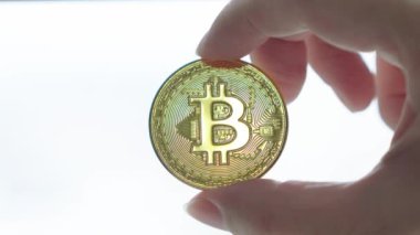 Parlak bir arkaplanda altın bir bitcoin tutan el, kripto para biriminin sembolik b sembolünü vurguluyor.