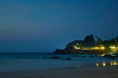 Lokanta, sıcak ışıklarıyla geceyi aydınlatırken deniz yavaşça kıyıya vuruyor.