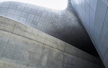 Mimari detay, beton duvarla eğri metal cephe arasındaki zıtlığı gösteriyor.