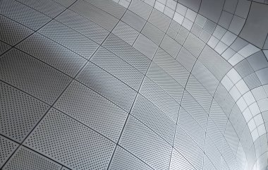 Delinmiş metal paneller modern mimaride eğri bir duvar oluşturuyor.