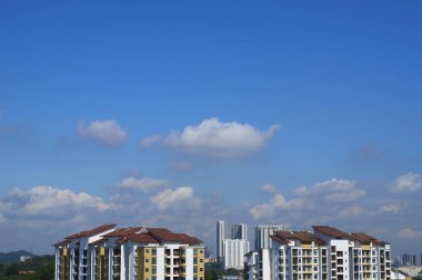 Çağdaş apartman kompleksleri canlı mavi bir gökyüzüne karşı dimdik dururlar. Kabarık beyaz bulutlar, şehir gelişimini ve modern yaşamı gözler önüne sererler.