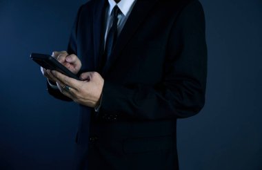 İşadamı, koyu mavi bir ortamda akıllı telefonunu kaydırıyor.