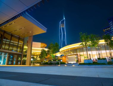 Modern buildings and a skyscraper are illuminated on an urban plaza at night