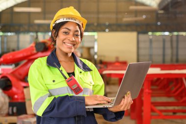 Professional female mechanical engineer worker in yellow hard hat and safety uniform controlling machinery standing at manufacturing area of industrial factory