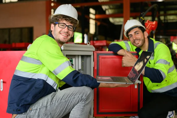 Happy industrial workers holding laptop working together at manufacturing factory