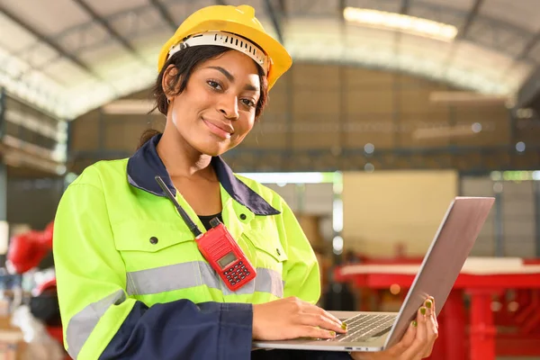 Professional female mechanical engineer worker in yellow hard hat and safety uniform controlling machinery standing at manufacturing area of industrial factory
