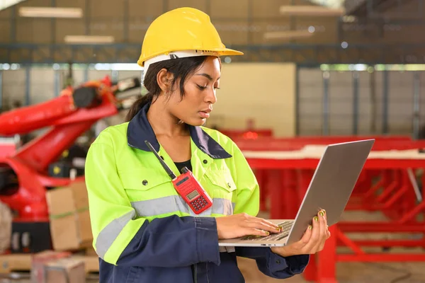Professional female mechanical engineer worker in yellow hard hat and safety uniform controlling machinery standing at manufacturing area of industrial factory