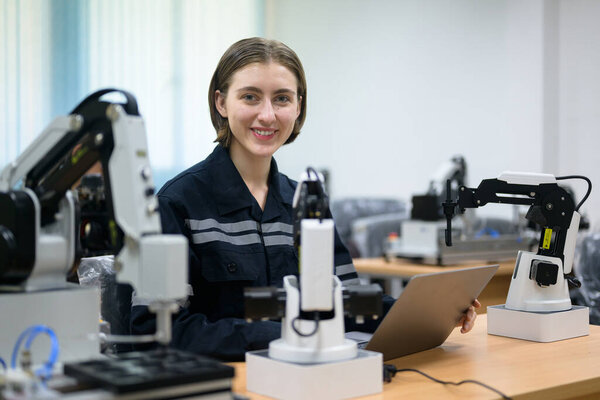 Female technician engineer using laptop checking and operating automatic robotic machine at industrial factory, Worker working with robotic system in factory