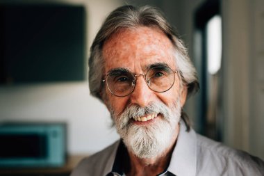 Portrait of healthy senior man with grey hair and beard looking at camera with smile, Retirement man resting and relaxing at home