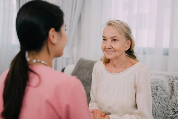 Senior patient with home care nurse, Happy senior woman talking with female caregiver in living room at home health care visit, Elderly care concept