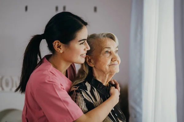 Senior patient with home care nurse, Happy senior woman talking with female caregiver in living room at home health care visit, Elderly care concept