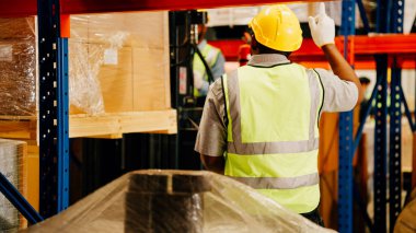 Depoda güvenlik kaskı kontrol eden ve kutuları kontrol eden depo çalışanları, forklift yükleyicisi, lojistik ve ticari ihracat konseptiyle karton kutuları taşıyan profesyonel depo çalışanları.