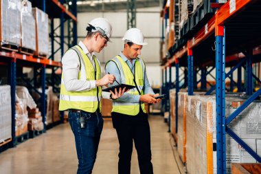 Smart male engineer manager wearing safety vest and helmet using digital tablet checking and assigning work to warehouse workers, Smart teamwork working concept