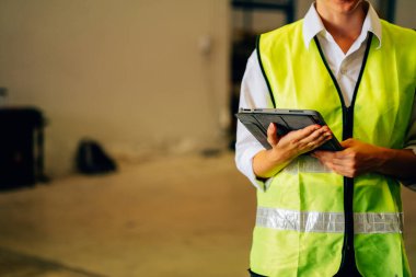 Happy warehouse engineer with safety vest using tablet for checking goods and supplies on shelves with goods background in warehouse store, Logistic and business export concept