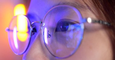 Close up view of woman wearing computer glasses for reducing eye strain blurred vision looking at pc screen with computer reflection, People playing games using internet and watching video at home