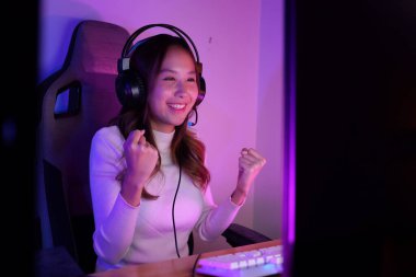 Winner gamer portrait, Young woman wearing headphones playing computer game, Female gamer winning hard match with happiness, Woman playing video game looking at computer monitor