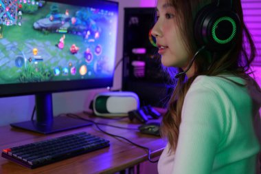 Genç bayan oyun kurucu evde bilgisayarda oyun oynuyor, kulaklık takan oyuncu kadın takım arkadaşlarıyla mikrofon takıyor, oyuncu yaşam tarzı, E-Sport online oyun teknolojisi