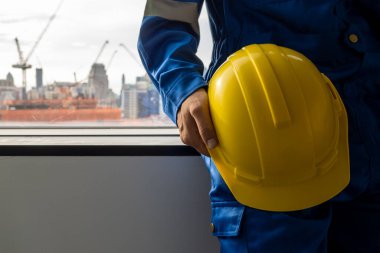Safety first helmet with engineer at construction site, Engineer holding yellow helmet with construction building site background