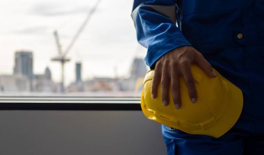 Safety first helmet with engineer at construction site, Engineer holding yellow helmet with construction building site background