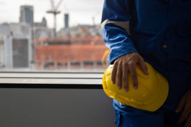 Safety first helmet with engineer at construction site, Engineer holding yellow helmet with construction building site background