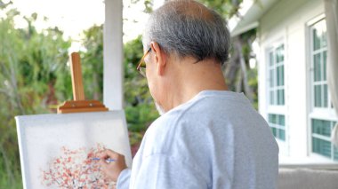 Senior painting picture, Old man drawing in garden, Senior holding color paint drawing on white paper, Elderly activities on free time. happy elderly. life after retirement concept