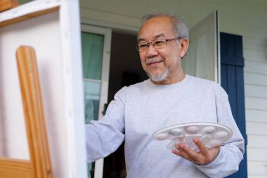 Senior painting picture, Old man drawing in garden, Senior holding color paint drawing on white paper, Elderly activities on free time, Happy elderly life after retirement concept