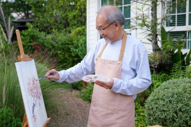 Senior painting picture, Old man drawing in garden, Senior holding color paint drawing on white paper, Elderly activities on free time, Happy elderly life after retirement concept
