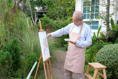Senior painting picture, Old man drawing in garden, Senior holding color paint drawing on white paper, Elderly activities on free time, Happy elderly life after retirement concept