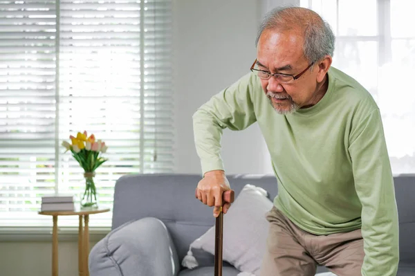 Elderly man using walking stick trying to stand and walk at home, Senior man with health problems using walking stick to walk at home