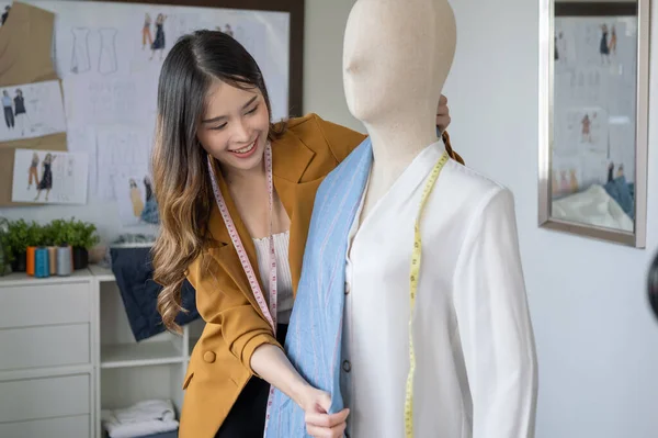 Happy female dressmaker cutting fabric on sketch line, Fashion designer stylist designing new clothes collection working in the fashion studio, Clothes business owner concept